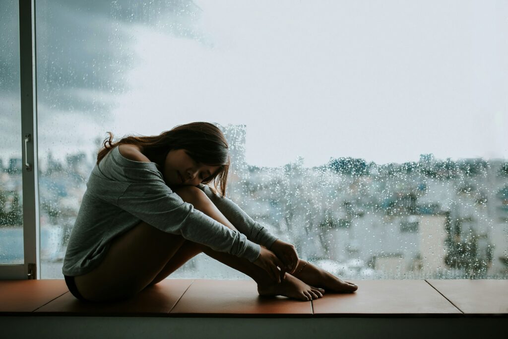 young woman sitting next to the window being sad